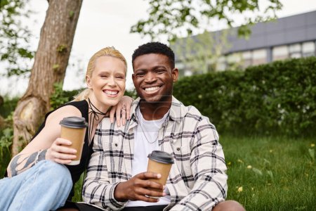 Multicultural couple, an African American man and a Caucasian woman, enjoying coffee together while seated on grass.