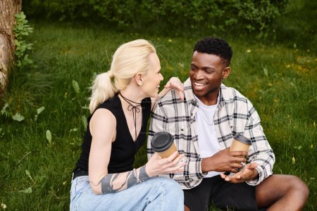 A happy multicultural couple, an African American man and a Caucasian woman, sitting together on the grass in a park.