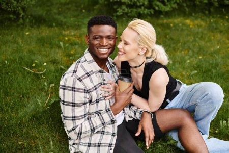 Un hombre afroamericano feliz y una mujer caucásica se sientan juntos en la hierba, disfrutando de la belleza del aire libre.