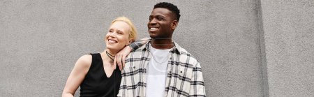 Téléchargez les photos : Un couple multiculturel se tient joyeusement côte à côte dans une rue urbaine près d'un bâtiment gris. - en image libre de droit