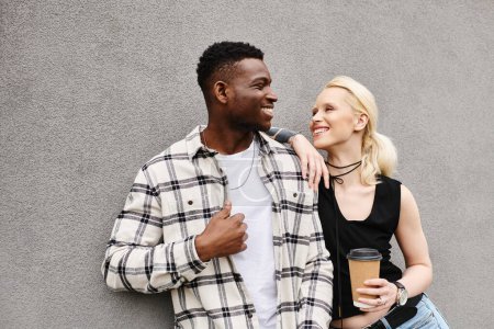 Una feliz pareja multicultural, un hombre y una mujer, están juntos cerca de un edificio gris en una calle urbana.