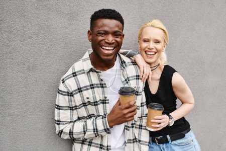 A multicultural couple enjoys a coffee break on an urban street, with the man standing next to the woman holding a cup of coffee.