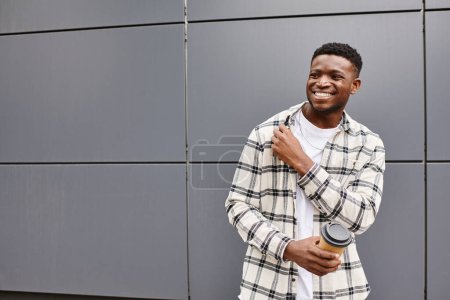 Foto de Hombre negro feliz de pie frente a una pared urbana gris, exudando felicidad. - Imagen libre de derechos