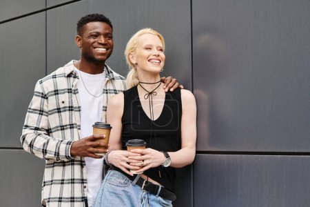 Un couple multiculturel, un homme et une femme, heureux ensemble dans une rue urbaine près d'un bâtiment gris.