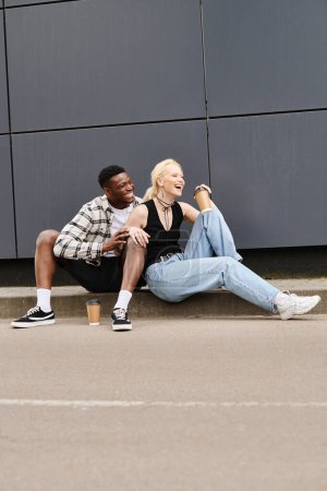 Un homme et une femme heureux multiculturels assis ensemble sur le sol près d'un bâtiment gris, profiter de leur temps à l'extérieur.