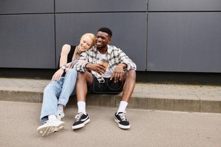 Téléchargez les photos : Un homme et une femme assis paisiblement sur le sol près d'un bâtiment gris dans un cadre urbain, profitant de l'autre compagnie. - en image libre de droit