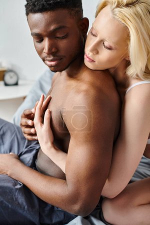 A sensual moment captured as a multicultural boyfriend and girlfriend embrace warmly and cuddle lovingly on a bed.