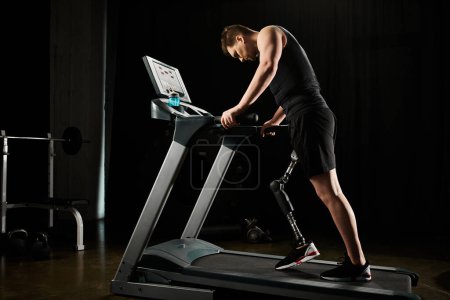 Foto de Un hombre con una pierna protésica trabaja en una cinta de correr en un gimnasio oscuro - Imagen libre de derechos