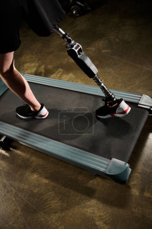 Un hombre discapacitado con una pierna protésica está de pie con confianza en la parte superior de una cinta de correr en el gimnasio, centrado en su entrenamiento.