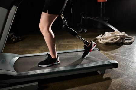 A person with a prosthetic leg is walking on a treadmill in a gym, showing determination and strength in their workout routine.