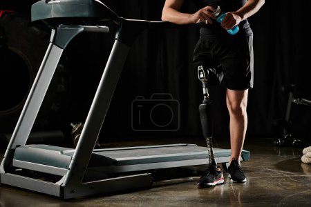 A disabled man with a prosthetic leg is standing on a treadmill in a dark room, focused on his workout routine.