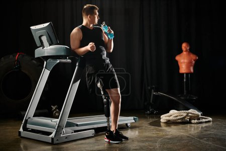 Téléchargez les photos : A man with a prosthetic leg stands on a treadmill, holding a bottle of water. - en image libre de droit