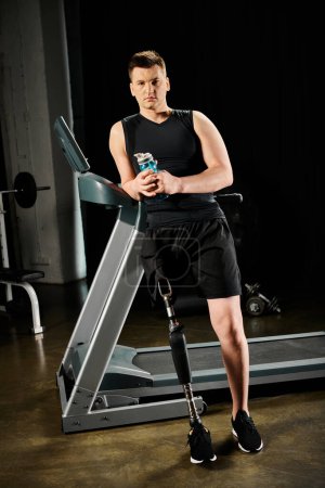 A man stands on a treadmill, holding a drink in his hand while working out at the gym with a prosthetic leg.