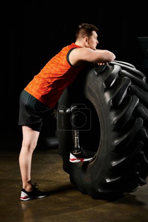 A man with a prosthetic leg stands next to a massive tire, ready to embark on a challenging workout routine.