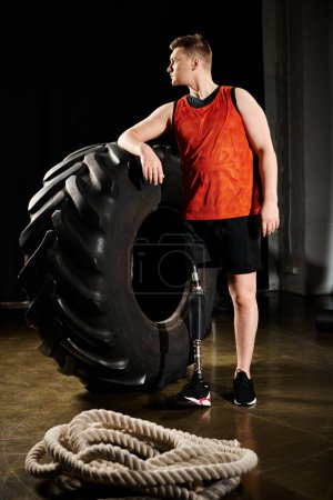 A man standing proudly next to a colossal tire, showcasing strength and determination in a moment of triumph.