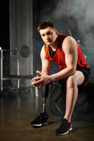 Photo for A man with a prosthetic leg sitting on top of a black tire in a gym, showcasing strength and determination - Royalty Free Image
