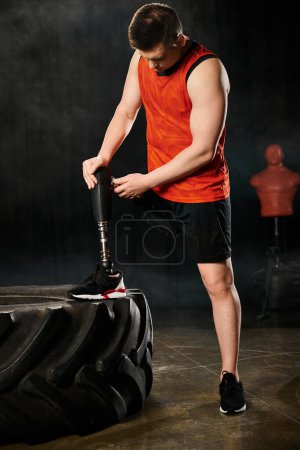 Ein Mann mit Beinprothese steht neben einem riesigen Reifen in einer Turnhalle.