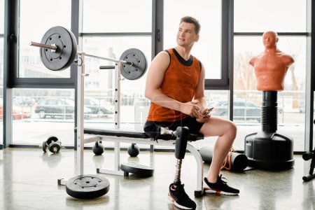 Un hombre discapacitado con una pierna protésica está sentado en un banco en un gimnasio, tomando un descanso de su rutina de entrenamiento.
