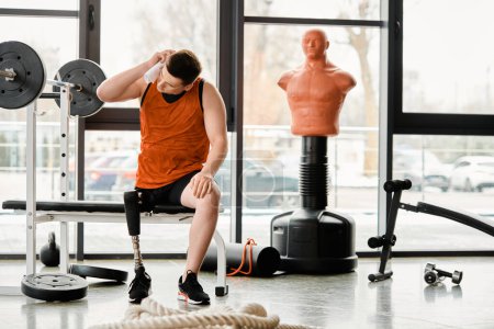 A disabled man with a prosthetic leg sitting on a bench in a gym, taking a moment to rest during his workout.