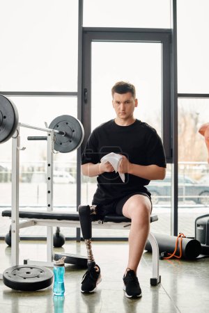 Téléchargez les photos : Un homme avec une prothèse de jambe s'assoit sur un banc dans une salle de gym, prenant un moment pour se reposer et réfléchir pendant son entraînement. - en image libre de droit