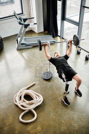 A disabled man with a prosthetic leg performs a deadlift in a gym, showcasing strength, determination, and resilience.