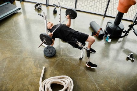 Un hombre determinado con una pierna protésica realiza un press de banca usando una barra en un gimnasio.