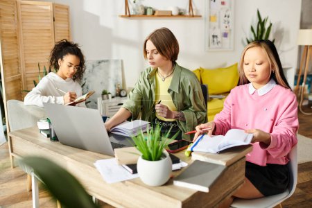 Drei interrassische Teenager-Mädchen in konzentrierter Studie sitzen an einem Tisch mit Laptops.