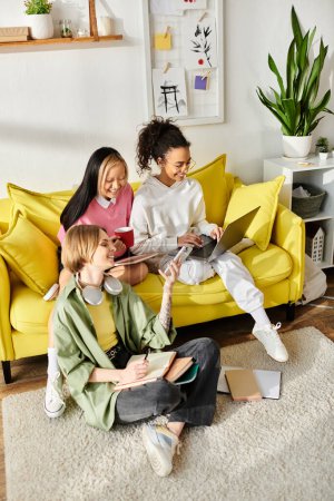 Foto de Un grupo diverso de chicas riendo mientras se sientan encima de un sofá amarillo brillante dentro de una habitación acogedora. - Imagen libre de derechos