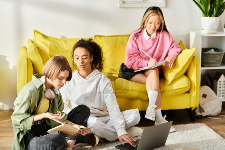 Foto de Grupo de adolescentes multirraciales sentadas en el suelo, absorbidas en estudiar juntas en el ordenador portátil en casa. - Imagen libre de derechos