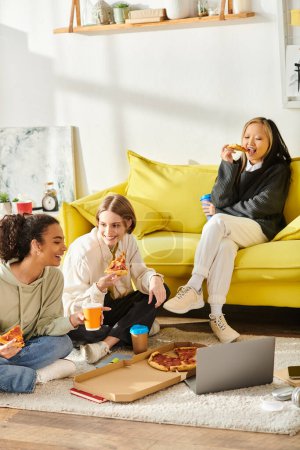 Multicultural teenage girls gathering on the floor, eating pizza, and sharing laughter at home.