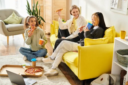Un grupo muy unido de adolescentes, de diferentes razas, sentadas cómodamente en un vibrante sofá amarillo en el interior.