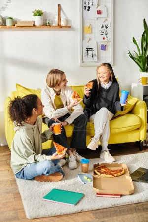 Adolescentes de diferentes razas sentadas en un sofá, disfrutando rebanadas de pizza juntas.