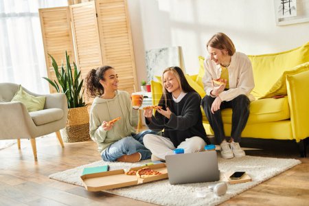 Un grupo diverso de adolescentes sentadas en el suelo, disfrutando de la pizza juntas en un acogedor entorno hogareño.