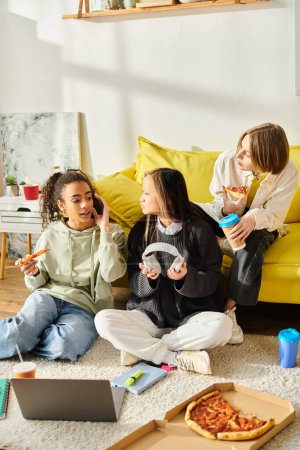 Three engaging teenage girls of different ethnic backgrounds enjoy a casual pizza feast while seated on the floor.