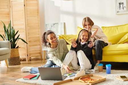 Teenager-Freundinnen mit unterschiedlichem Hintergrund sitzen auf dem Fußboden, vertieft in den Laptop-Bildschirm.