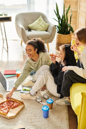 Téléchargez les photos : Groupe diversifié d'adolescentes assis autour d'une table, dégustant une pizza ensemble à la maison. - en image libre de droit