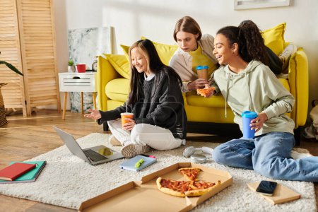 Interrassische Teenager-Mädchen genießen zusammen Pizza, sitzen auf dem Boden und teilen eine Mahlzeit in einem gemütlichen, heimeligen Ambiente.