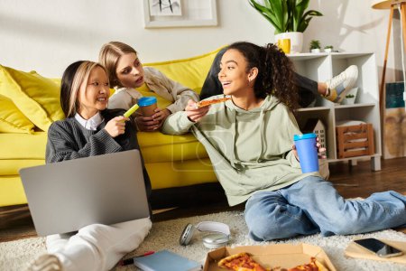 Téléchargez les photos : Un groupe diversifié d'adolescentes dégustant des pizzas tout en étant assis sur le sol, collant sur la nourriture et l'amitié. - en image libre de droit