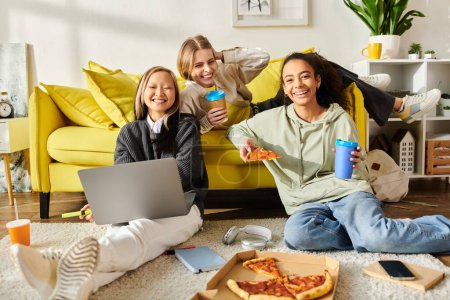 Foto de Tres chicas adolescentes de diferentes razas se sientan en el suelo, disfrutando de pizza y refrescos mientras charlan y ríen. - Imagen libre de derechos