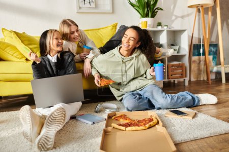 Diverse Gruppe Teenager-Mädchen sitzen zusammen auf dem Fußboden und genießen Pizza in gemütlicher Atmosphäre zu Hause.