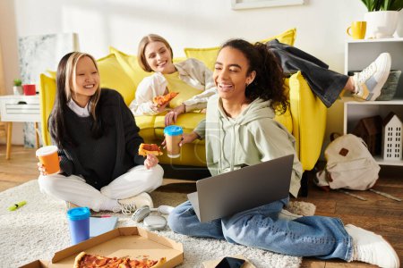 Téléchargez les photos : Un groupe diversifié d'adolescentes assises sur le sol mangeant joyeusement de la pizza ensemble. - en image libre de droit