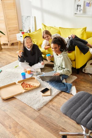 Foto de Un grupo diverso de adolescentes de diferentes etnias se sientan en el suelo en una cálida sala de estar, charlando y riendo. - Imagen libre de derechos