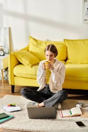 Photo for A teenage girl sits on the floor with a cup of coffee while engaging in e-learning with her laptop at home. - Royalty Free Image