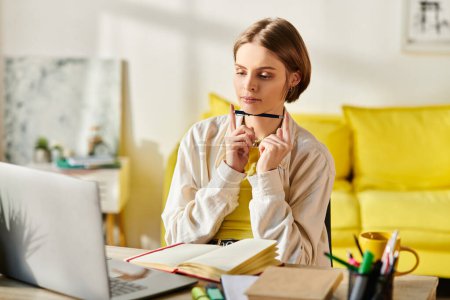 Une adolescente assise avec attention devant son ordinateur portable, absorbée par l'apprentissage en ligne et les études à la maison.