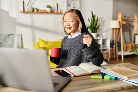 Photo for A young Asian girl immersed in online learning, sitting at a table with a laptop and a book. - Royalty Free Image