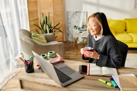 Una joven asiática se sienta en una mesa con una computadora portátil, absorta en el estudio en línea mientras toma café.