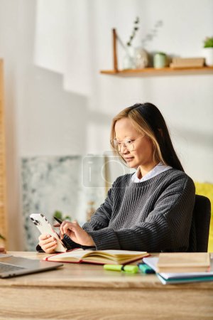 Eine junge Asiatin sitzt an einem Schreibtisch und beschäftigt sich mit E-Learning auf ihrem Handy.