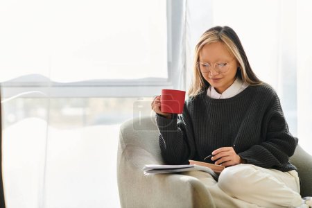 A young Asian woman enjoys a quiet moment, sitting on a couch with a cup of coffee in her hand
