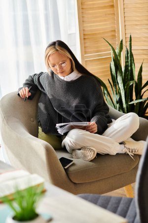 Una joven asiática se sumerge en un libro mientras se sienta cómodamente en una silla en casa