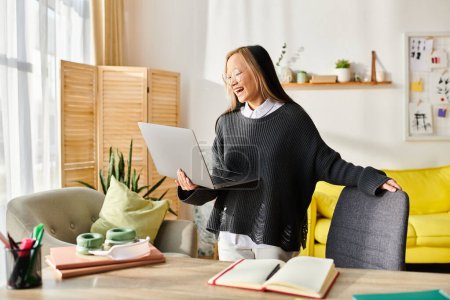 A young Asian girl stands confidently in a living room, engrossed in her studies while holding a laptop.